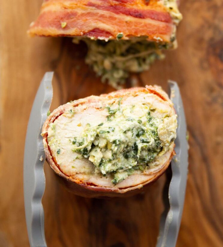 close up overhead shot of tongs holding sliced chicken showing spinach artichoke filling
