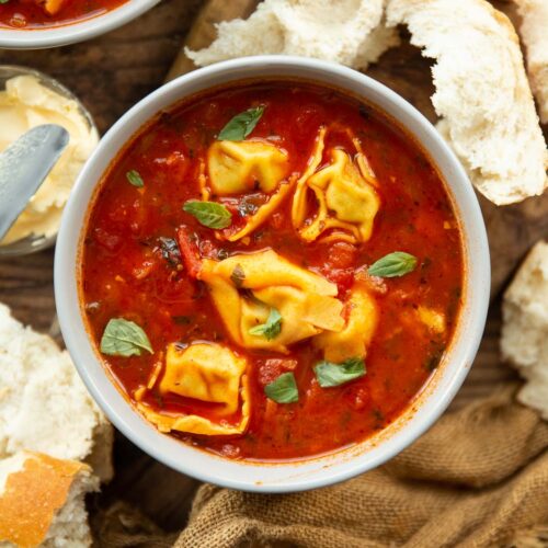 overhead shot of tomato tortellini soup in bowl surrounded by chunks of bread