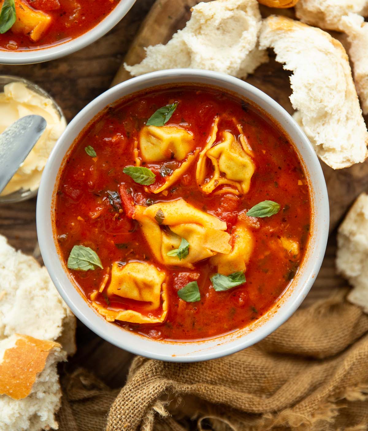 overhead shot of tomato tortellini soup in bowl surrounded by chunks of bread