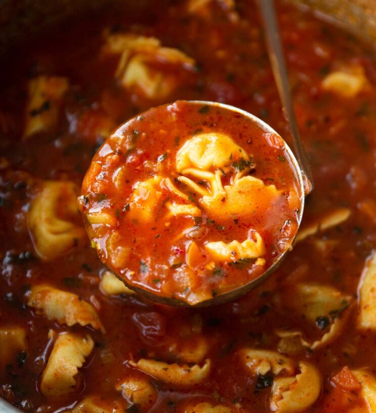 silver ladle scooping tortellini soup out of large pot