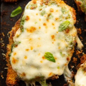 close up overhead shot of baked pesto chicken fresh out the oven on black baking tray