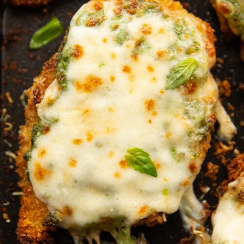 close up overhead shot of baked pesto chicken fresh out the oven on black baking tray