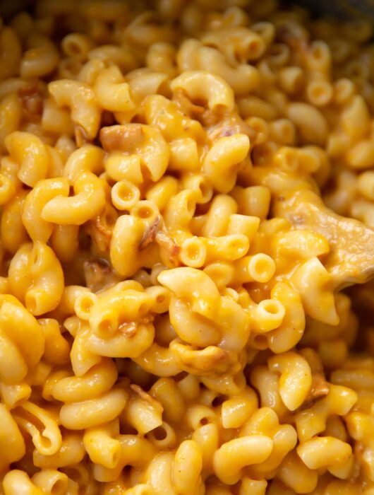 close up shot of butternut squash mac and cheese in pot with wooden spoon digging in