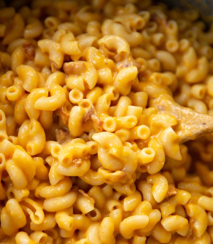 close up shot of butternut squash mac and cheese in pot with wooden spoon digging in