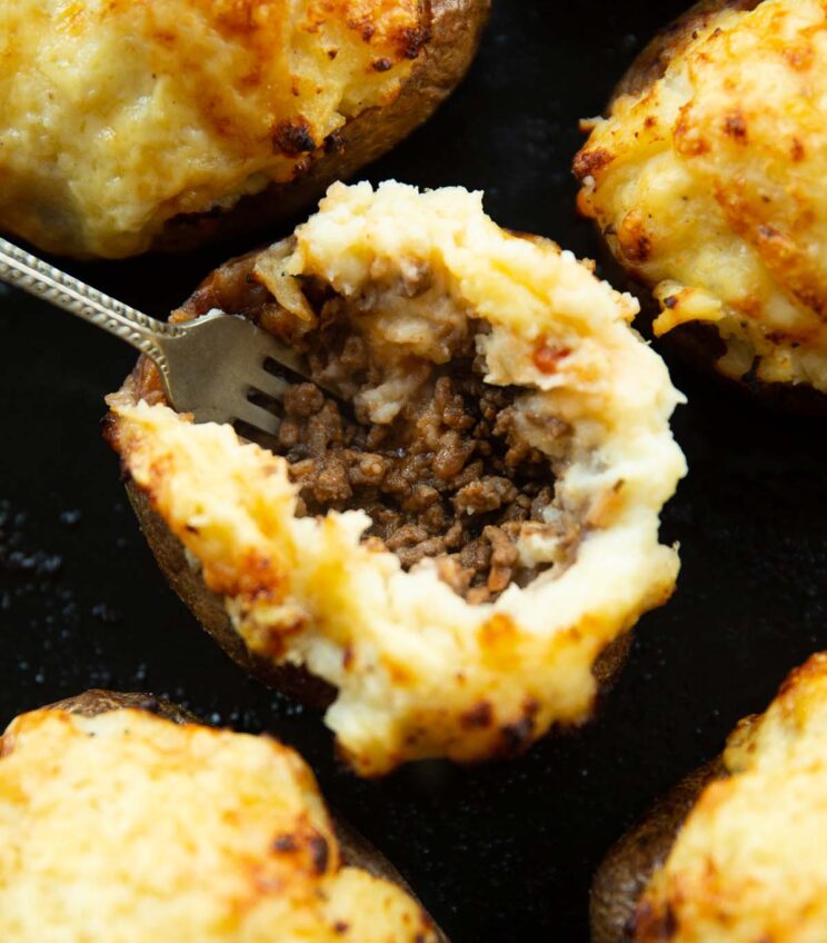 close up shot of silver fork digging in to cottage pie baked potato on baking tray