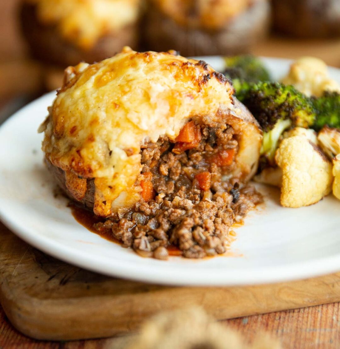 cottage pie loaded potato sliced in half on small white plate with roasted broccoli and cauliflower