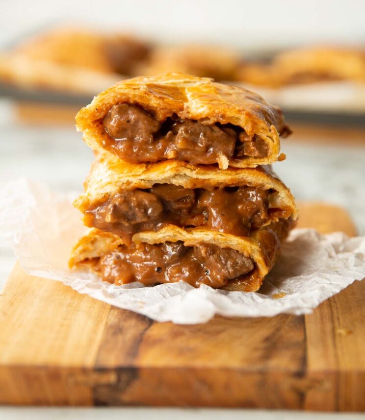 3 Greggs steak bakes stacked on each other on wooden chopping board