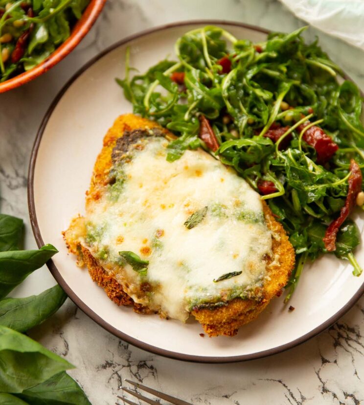 pesto baked chicken on small white plate with side salad