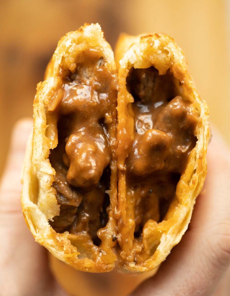 overhead close up shot of hand holding two steak bake halves showing filling