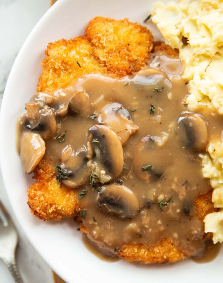 overhead close up shot of chicken schnitzel with mushroom gravy and mashed potato on white plate