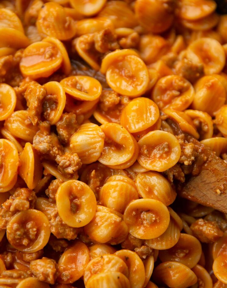 close up shot of wooden spoon digging into pan of sausage orecchiette