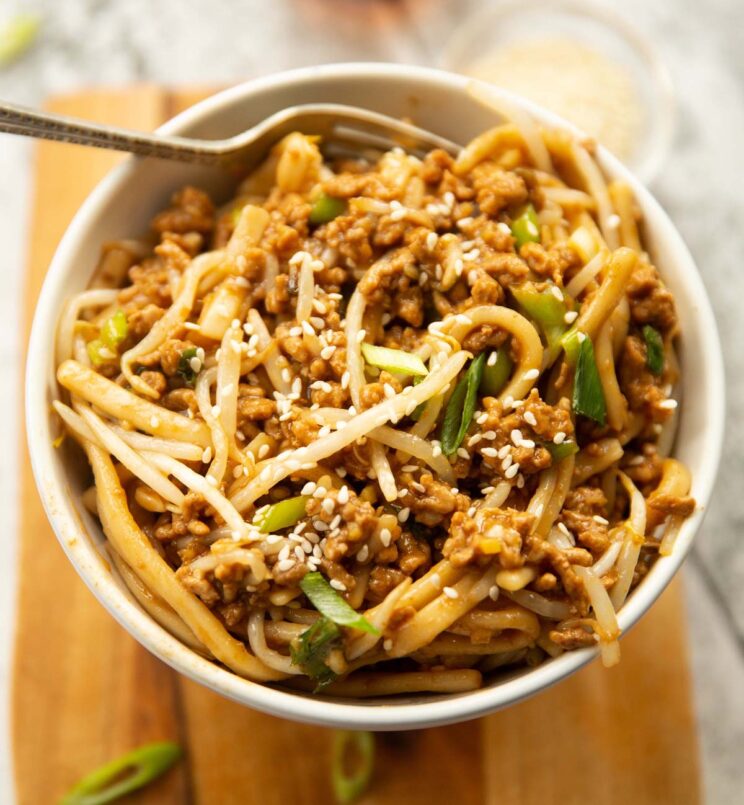 close up shot of spicy ground pork noodles in small white bowl on wooden chopping board