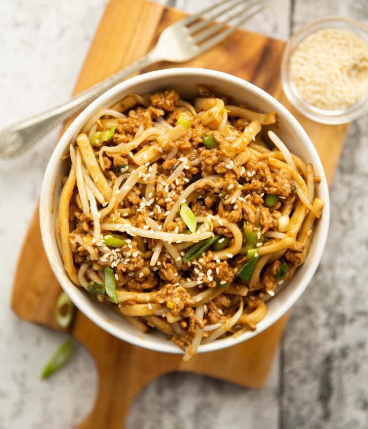 overhead shot of spicy hoisin pork noodles in small white bowl on chopping board