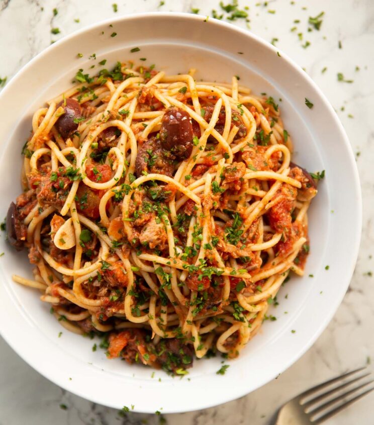 overhead shot of tuna puttanesca pasta in large white bowl garnished with fresh parsley
