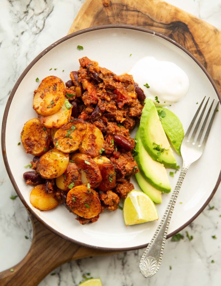overhead shot of chilli beef hotpot on small white plate with sour cream and sliced avocado