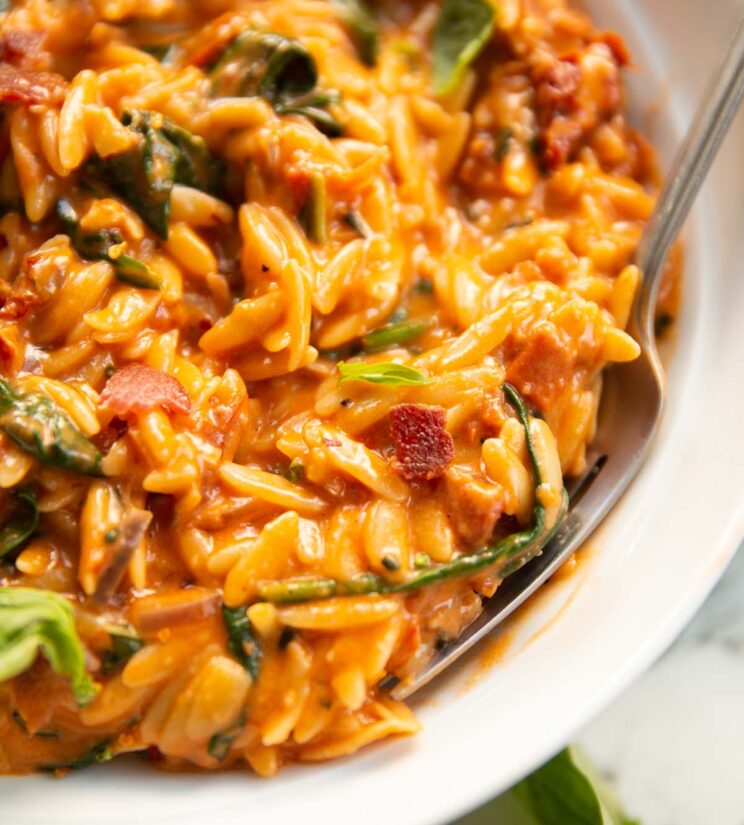 close up shot of spinach bacon tomato orzo in white dish with silver fork digging in