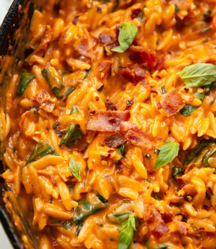 close up shot of tomato bacon spinach orzo in large cast-iron skillets