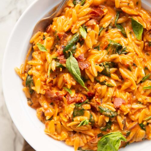 overhead shot of tomato spinach bacon orzo in large whit bowl with silver fork