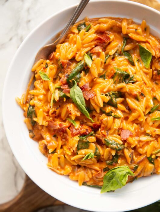 overhead shot of tomato spinach bacon orzo in large whit bowl with silver fork