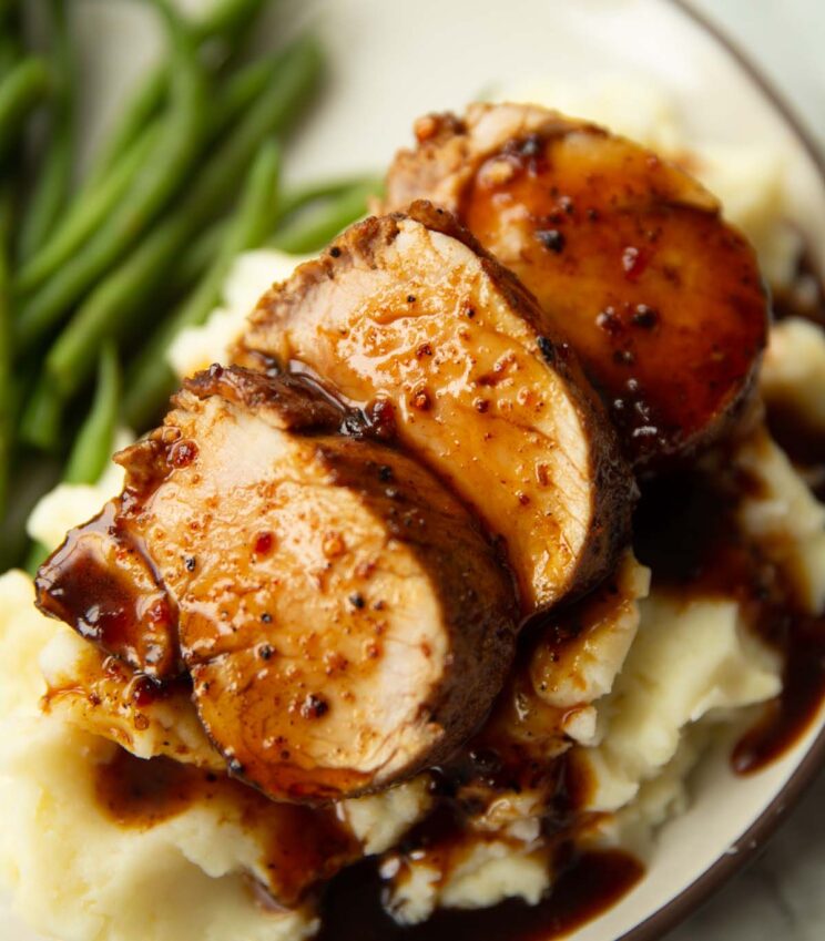 close up shot of sliced cajun honey butter pork tenderloin on mashed potatoes served with green beans