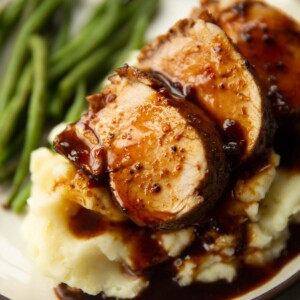 close up shot of sliced cajun pork tenderloin on mashed potatoes with green beans