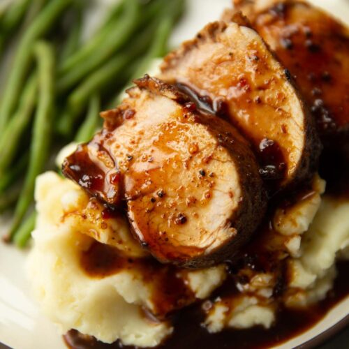 close up shot of sliced cajun pork tenderloin on mashed potatoes with green beans