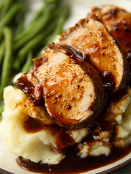 close up shot of sliced cajun pork tenderloin on mashed potatoes with green beans