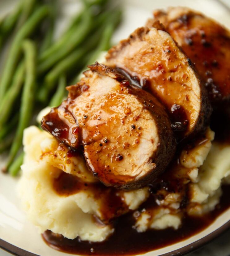 close up shot of sliced cajun pork tenderloin on mashed potatoes with green beans