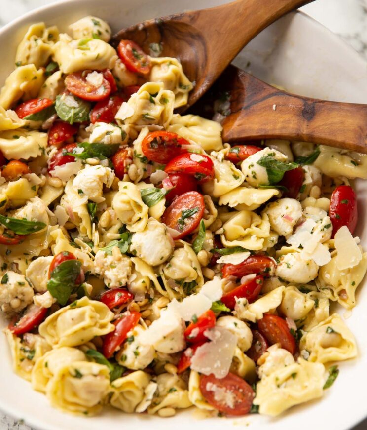 caprese tortellini pasta salad in large white bowl with brown salad tossers