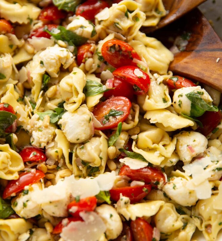 close up shot of caprese tortellini salad in large bowl with salad tossers