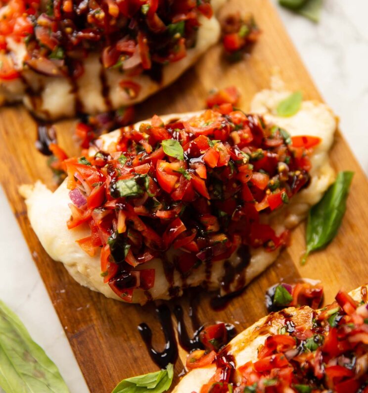close up shot of chicken bruschetta on wooden board with fresh basil as garnish