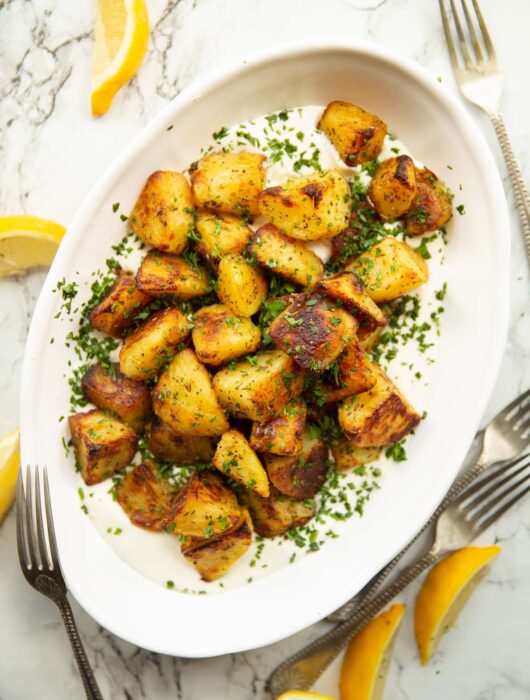 overhead shot of Greek roasted potatoes on whipped feta in white serving dish