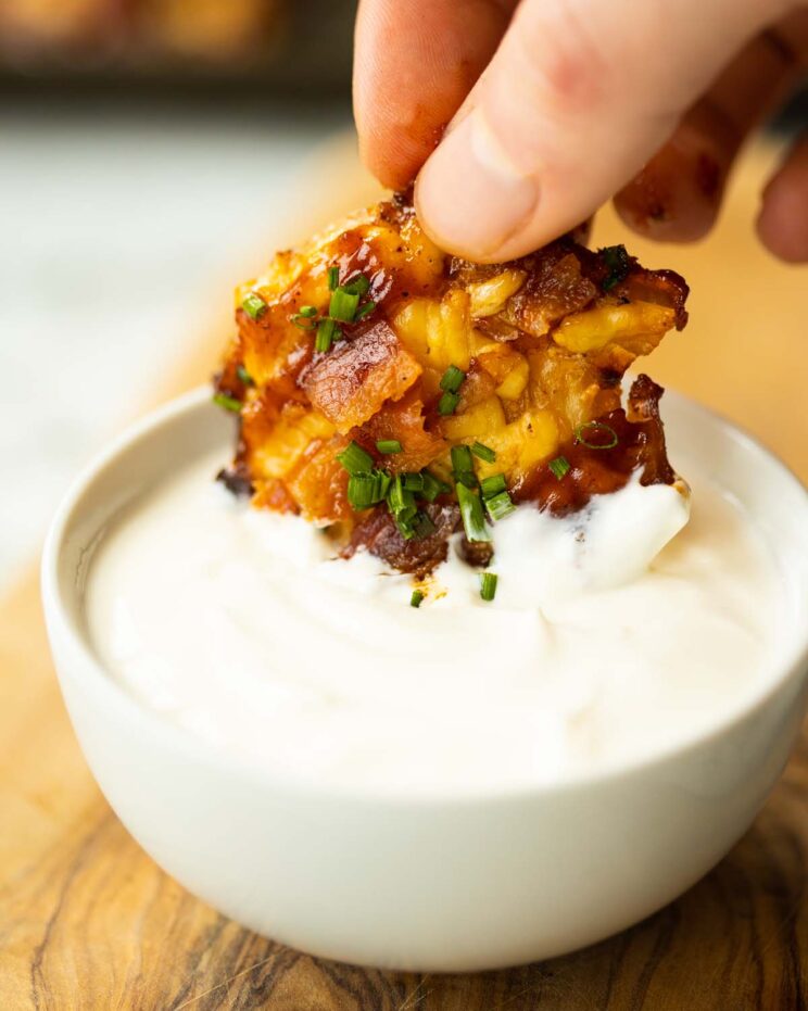 close up shot of hand dunking smashed potato into small white pot of sour cream