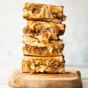 4 patty melt halves stacked on each other on wooden chopping board
