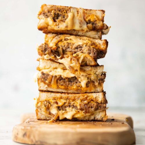 4 patty melt halves stacked on each other on wooden chopping board