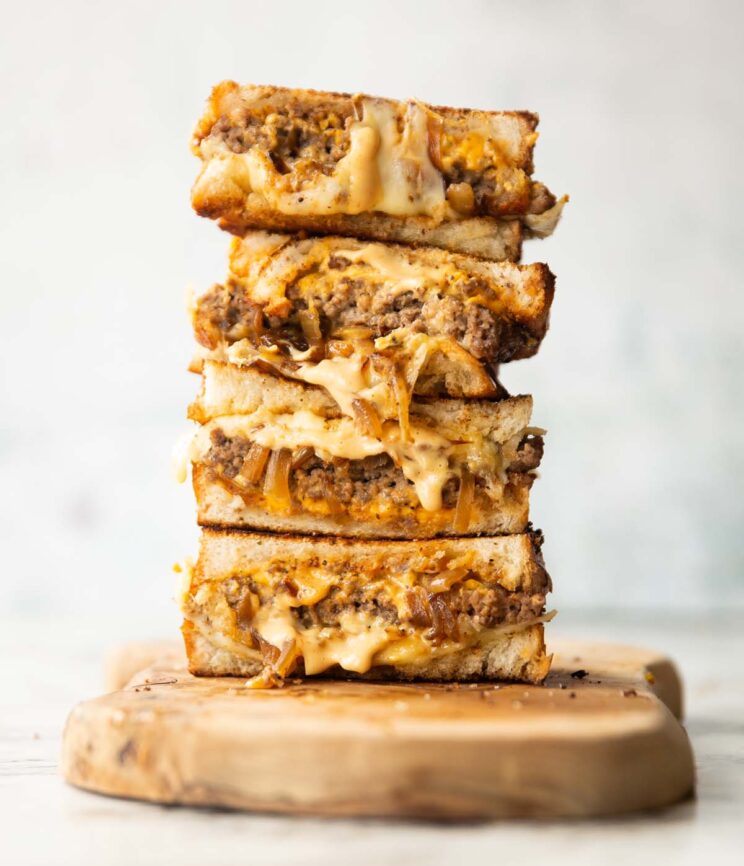 4 patty melt halves stacked on each other on wooden chopping board