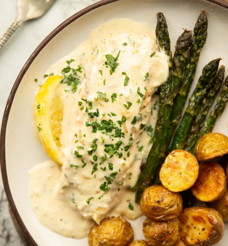 overhead shot of creamy lemon salmon on small white plate with roast potatoes and asparagus