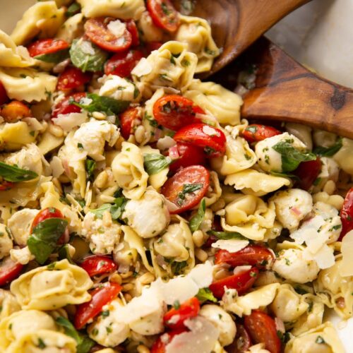 tortellini pasta salad in large white bowl with salad tossers at the back