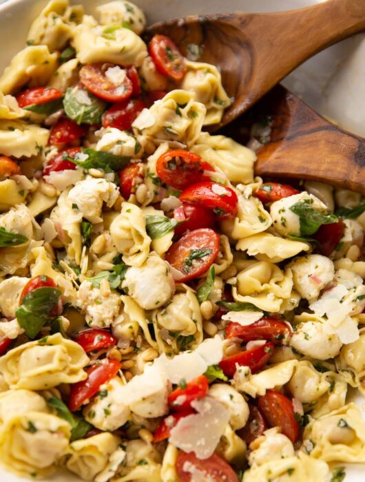 tortellini pasta salad in large white bowl with salad tossers at the back