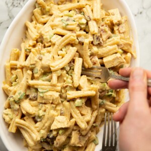 overhead shot of coronation chicken and bacon pasta salad in large oval dish with forks surrounding