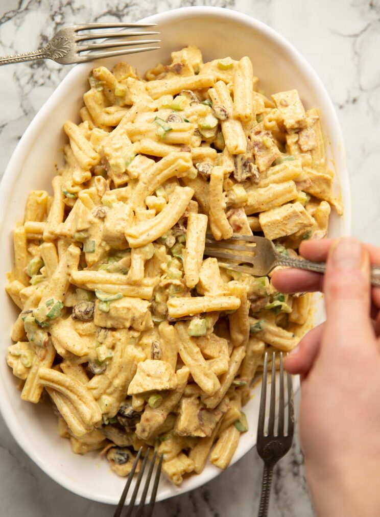 overhead shot of coronation chicken and bacon pasta salad in large oval dish with forks surrounding