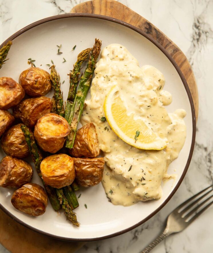 overhead shot of creamy lemon pork on small white plate with roast potatoes and asparagus