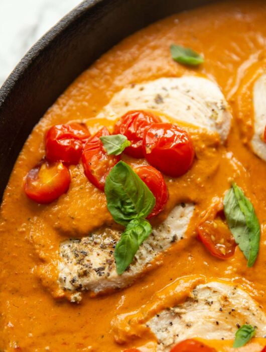 close up shot of creamy tomato chicken in pan garnished with basil