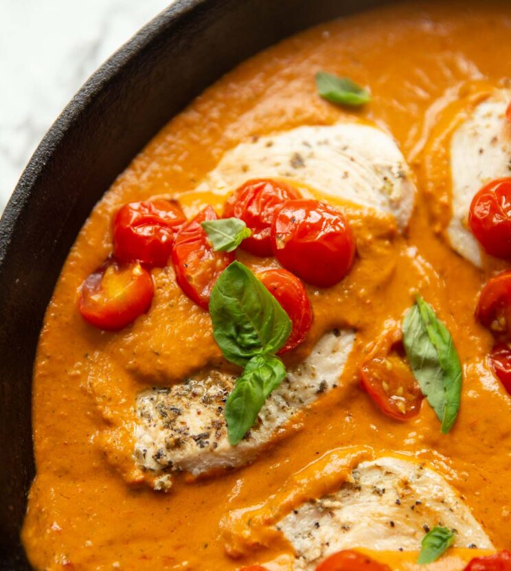 close up shot of creamy tomato chicken in pan garnished with basil