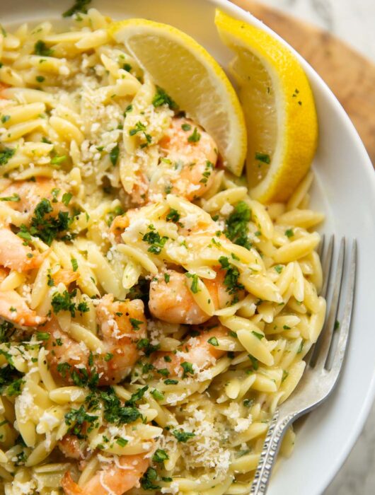close up shot of garlic butter orzo in large white plate with silver fork