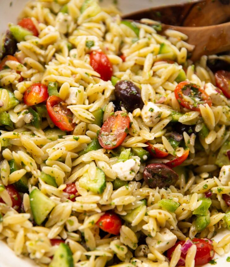close up shot of greek orzo salad in large salad bowl with salad tossers
