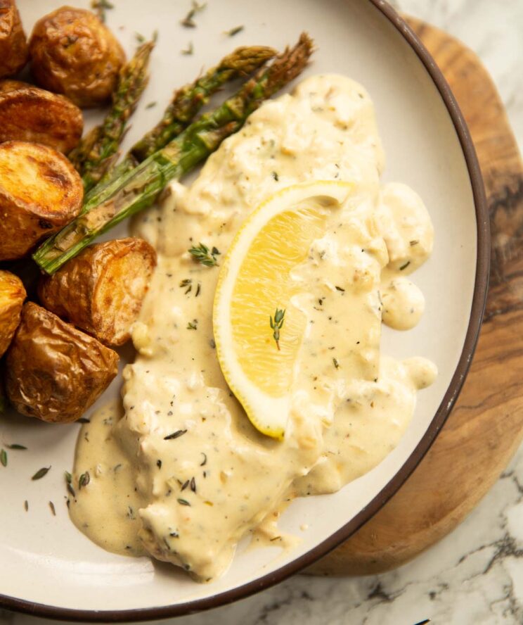 close up shot of lemon thyme pork chop on small white plate with potatoes and asparagus