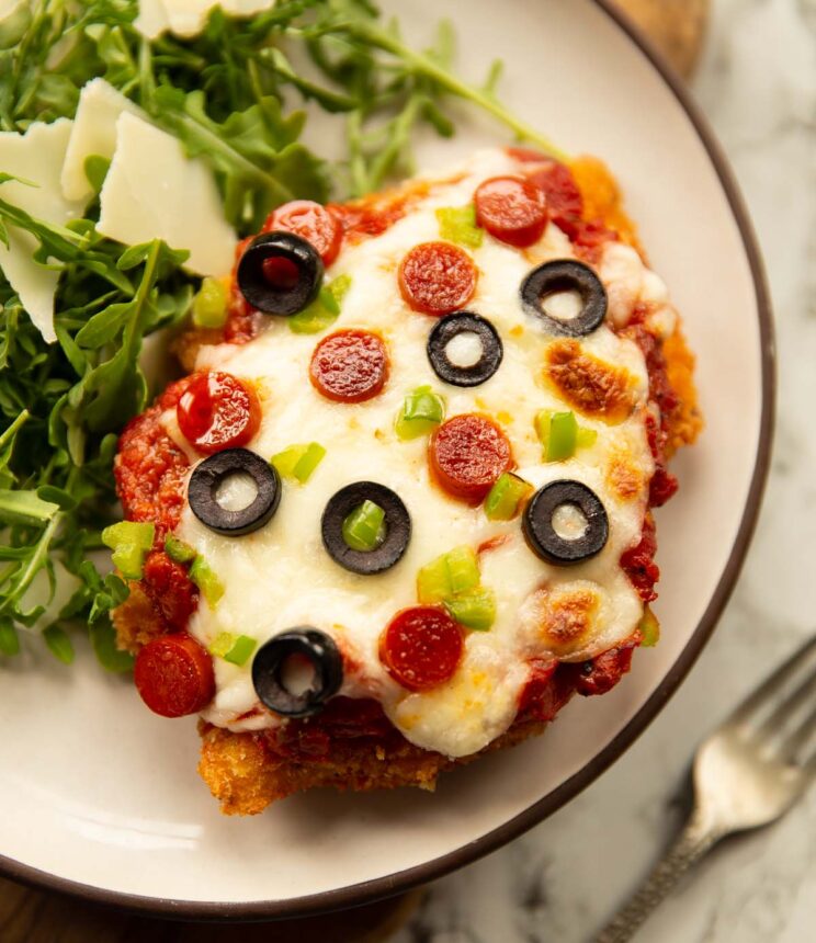 close up shot of pizza chicken parmesan on small white plate with rocket salad