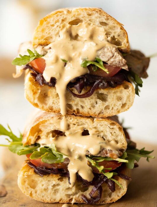 two steak sandwiches stacked on each other with sauce dripping out