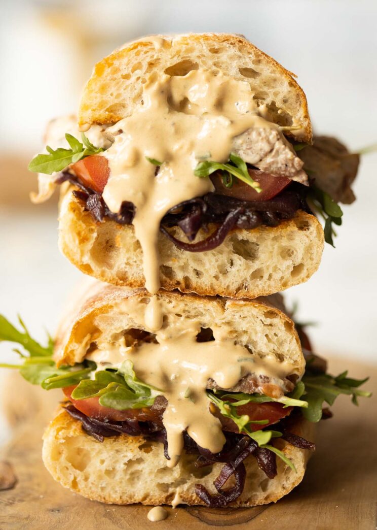two steak sandwiches stacked on each other with sauce dripping out
